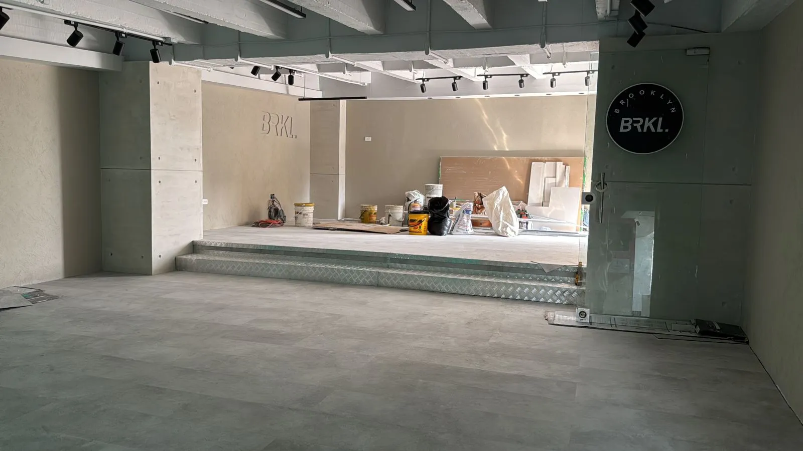 Espacio comercial amplio con pisos en porcelanato gris claro, iluminación riel y acabados en concreto