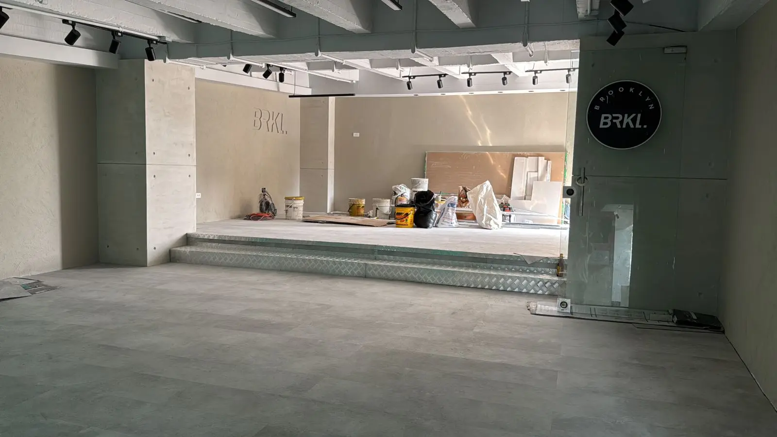 Espacio comercial amplio con pisos en porcelanato gris claro, iluminación riel y acabados en concreto